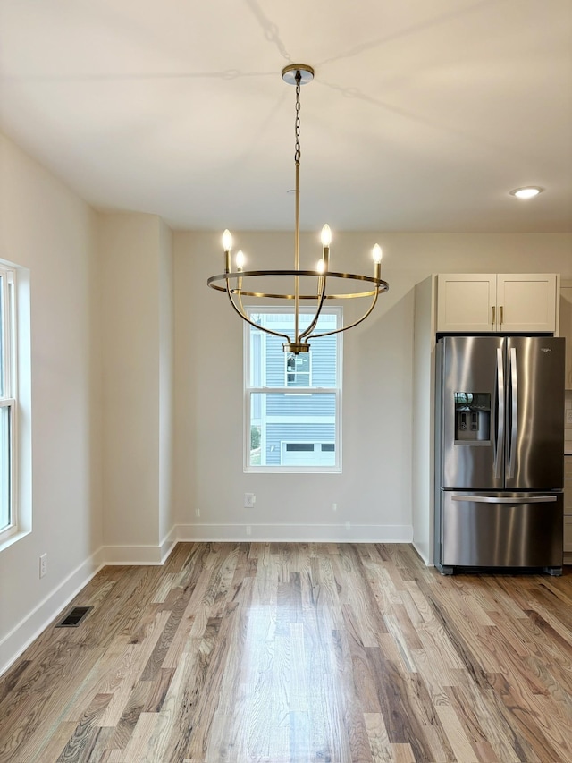 unfurnished dining area with an inviting chandelier and light hardwood / wood-style floors