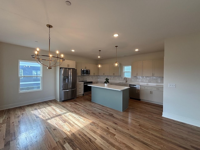 kitchen featuring appliances with stainless steel finishes, decorative light fixtures, tasteful backsplash, sink, and a center island