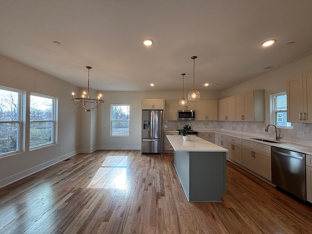 kitchen with sink, tasteful backsplash, hanging light fixtures, appliances with stainless steel finishes, and a kitchen island