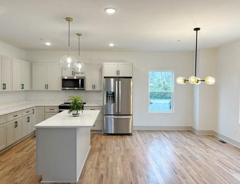 kitchen with light hardwood / wood-style flooring, hanging light fixtures, backsplash, stainless steel appliances, and a kitchen island