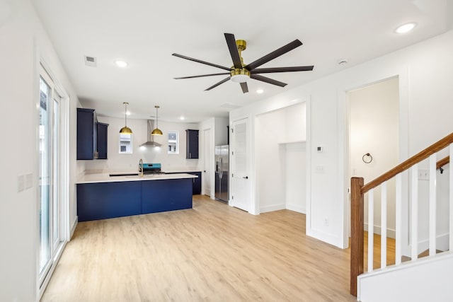 kitchen featuring stainless steel refrigerator with ice dispenser, a breakfast bar area, hanging light fixtures, hardwood / wood-style floors, and wall chimney range hood