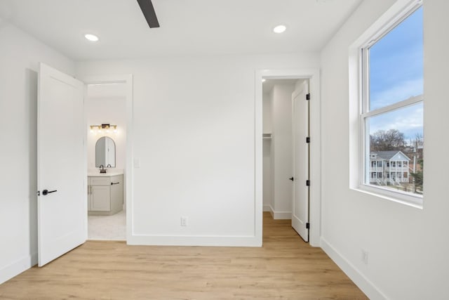 unfurnished bedroom featuring ceiling fan, a spacious closet, sink, and light wood-type flooring