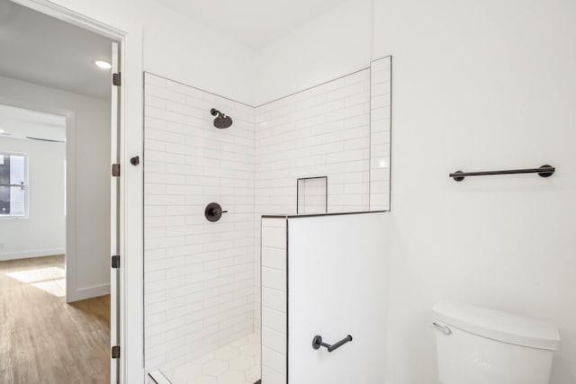 bathroom with hardwood / wood-style floors, a tile shower, and toilet