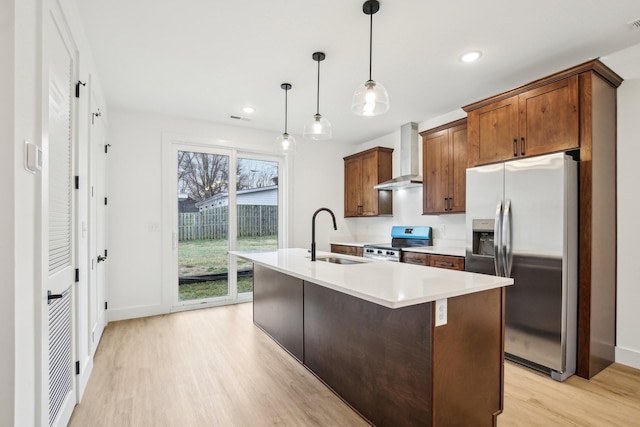 kitchen featuring wall chimney exhaust hood, sink, hanging light fixtures, stainless steel appliances, and a kitchen island with sink