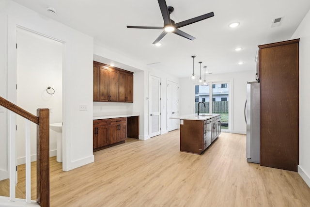 kitchen with pendant lighting, light hardwood / wood-style flooring, ceiling fan, a kitchen island with sink, and stainless steel appliances