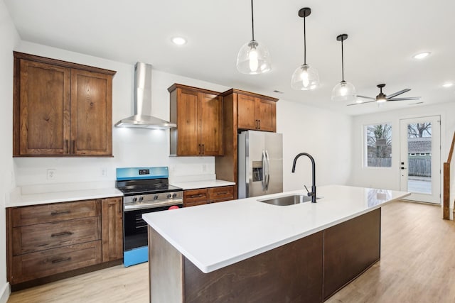 kitchen featuring pendant lighting, sink, appliances with stainless steel finishes, a center island with sink, and wall chimney exhaust hood