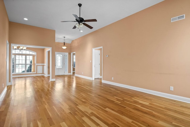 unfurnished living room with a towering ceiling, ceiling fan with notable chandelier, and light wood-type flooring