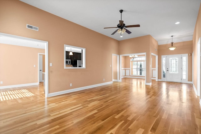 unfurnished living room with a high ceiling, ceiling fan with notable chandelier, and light wood-type flooring