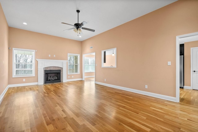 unfurnished living room with ceiling fan, a tiled fireplace, and light wood-type flooring