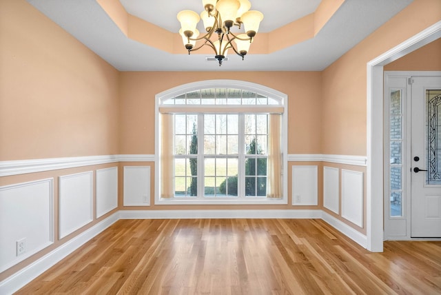 empty room featuring a raised ceiling, a chandelier, and light hardwood / wood-style flooring