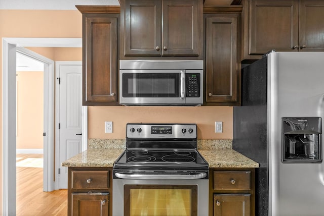 kitchen with stainless steel appliances, light stone countertops, and dark brown cabinets