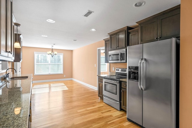 kitchen featuring pendant lighting, dark stone counters, light hardwood / wood-style floors, dark brown cabinetry, and stainless steel appliances