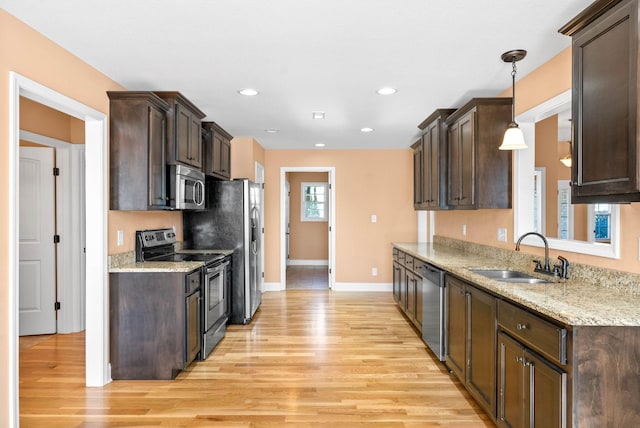 kitchen featuring pendant lighting, sink, stainless steel appliances, light stone countertops, and light wood-type flooring