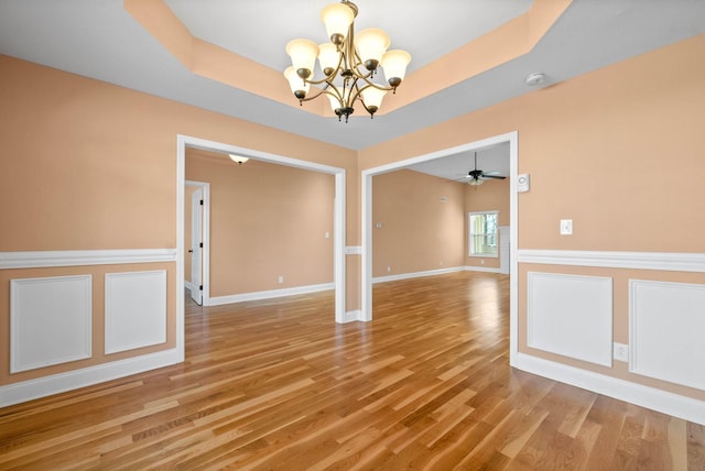 spare room featuring ceiling fan with notable chandelier, a tray ceiling, and light hardwood / wood-style floors