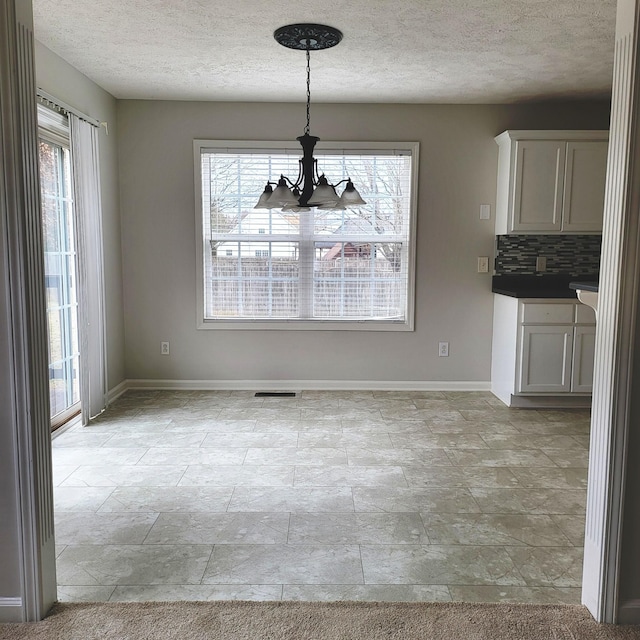 unfurnished dining area with plenty of natural light, a chandelier, and a textured ceiling