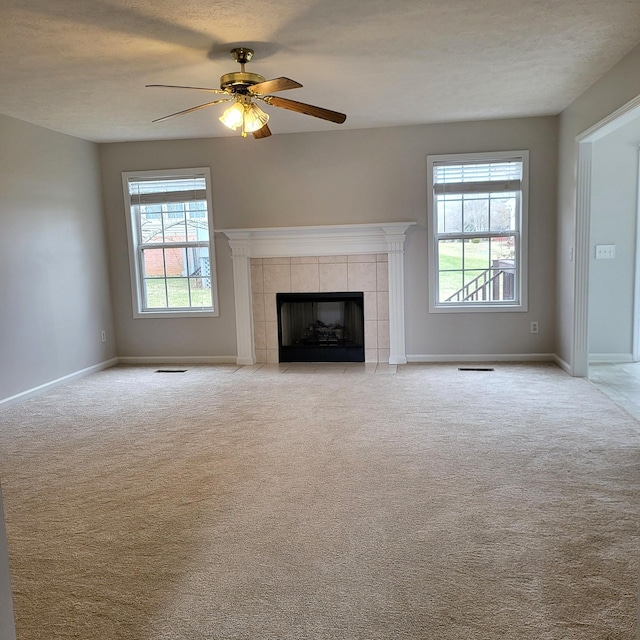 unfurnished living room featuring ceiling fan, light colored carpet, a tiled fireplace, and a textured ceiling