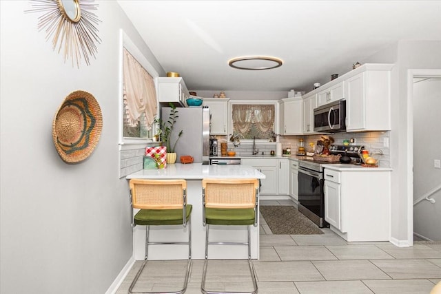 kitchen featuring a breakfast bar, white cabinetry, appliances with stainless steel finishes, kitchen peninsula, and decorative backsplash