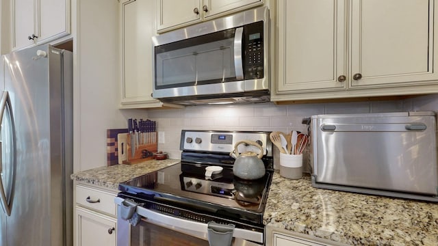 kitchen featuring light stone counters, decorative backsplash, and stainless steel appliances