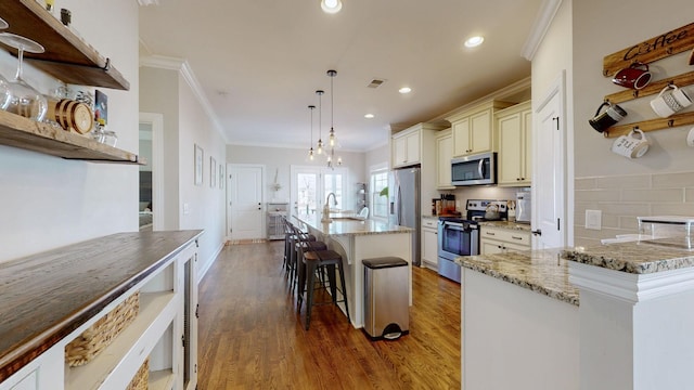 kitchen with sink, appliances with stainless steel finishes, hardwood / wood-style floors, a center island with sink, and decorative light fixtures