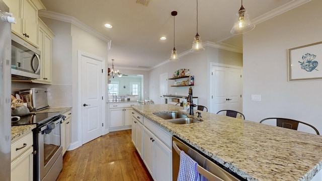 kitchen featuring an island with sink, sink, hanging light fixtures, stainless steel appliances, and light stone countertops