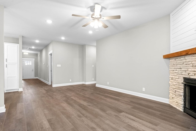 unfurnished living room featuring dark wood-type flooring, ceiling fan, and a stone fireplace