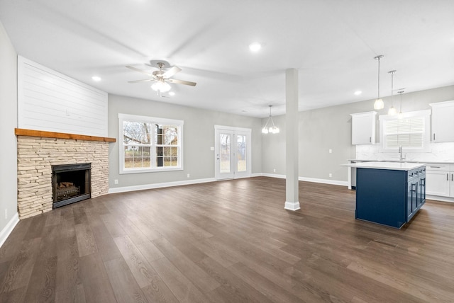 unfurnished living room featuring dark wood-type flooring, sink, a stone fireplace, and ceiling fan with notable chandelier