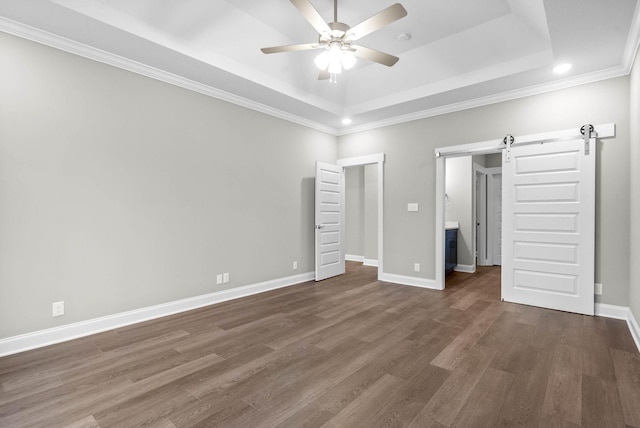 unfurnished bedroom with crown molding, ceiling fan, a tray ceiling, dark hardwood / wood-style flooring, and a barn door