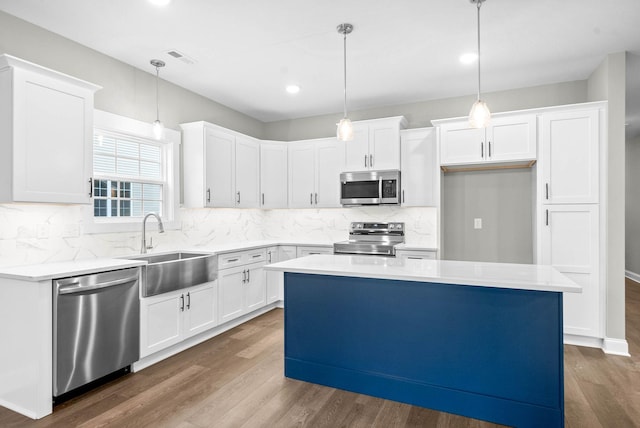 kitchen featuring appliances with stainless steel finishes, white cabinetry, sink, hanging light fixtures, and a center island