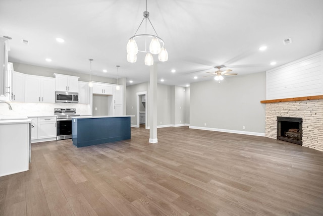 unfurnished living room with ceiling fan, a stone fireplace, sink, and light hardwood / wood-style flooring