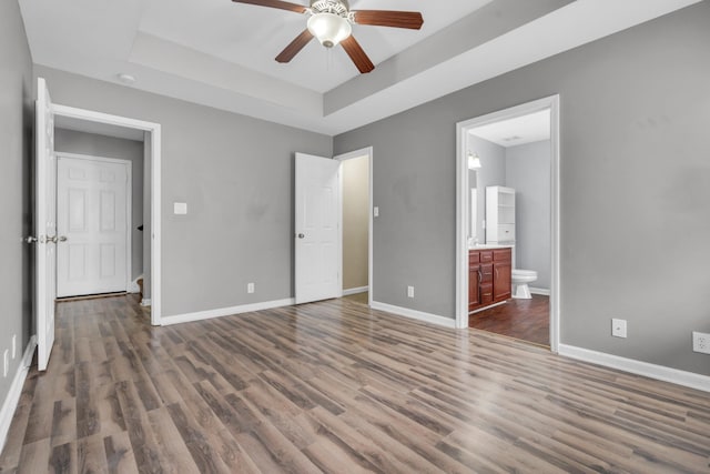 unfurnished bedroom with ensuite bathroom, ceiling fan, a tray ceiling, and dark hardwood / wood-style flooring