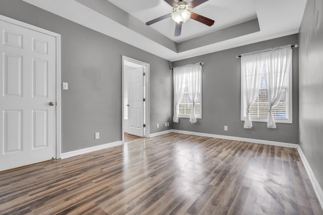 unfurnished room with ceiling fan, a wealth of natural light, a tray ceiling, and dark hardwood / wood-style flooring