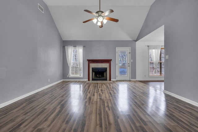 unfurnished living room with high vaulted ceiling, ceiling fan, a tiled fireplace, and dark wood-type flooring