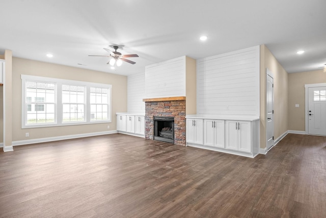 unfurnished living room with dark hardwood / wood-style floors, ceiling fan, and a stone fireplace