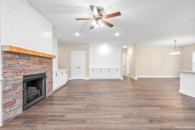 unfurnished living room featuring wood-type flooring, a stone fireplace, and ceiling fan with notable chandelier