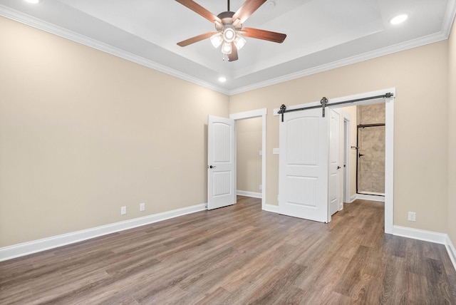 unfurnished bedroom featuring crown molding, a raised ceiling, ceiling fan, a barn door, and hardwood / wood-style floors