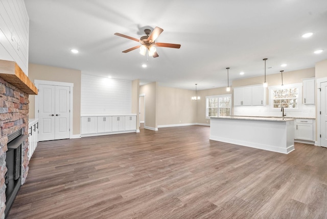 unfurnished living room with hardwood / wood-style flooring, a large fireplace, and ceiling fan with notable chandelier