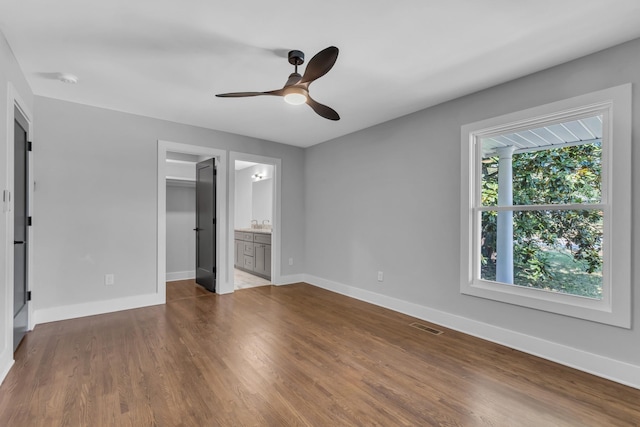 unfurnished bedroom with wood-type flooring, a walk in closet, ceiling fan, ensuite bath, and a closet