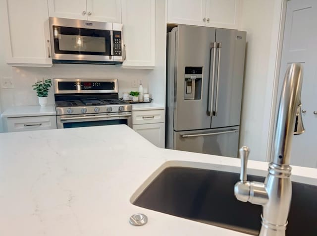 kitchen with stainless steel appliances, white cabinets, and light stone counters