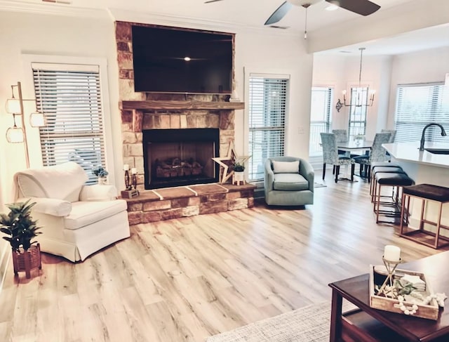 living room featuring ceiling fan with notable chandelier, light hardwood / wood-style floors, sink, and ornamental molding