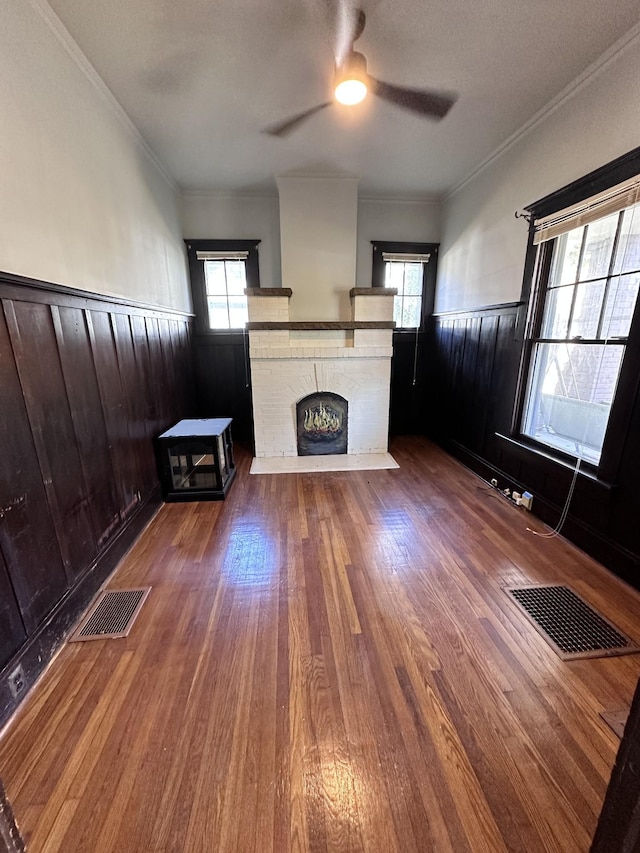 unfurnished living room featuring a fireplace, ornamental molding, dark hardwood / wood-style floors, and ceiling fan