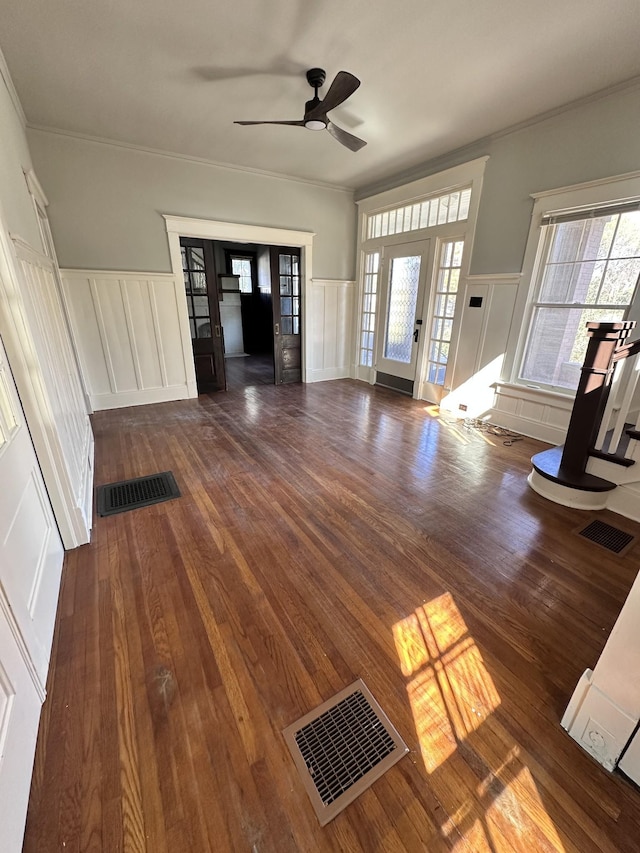 unfurnished living room featuring crown molding, plenty of natural light, dark wood-type flooring, and ceiling fan