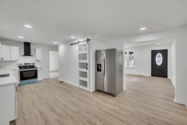 kitchen with appliances with stainless steel finishes, white cabinets, light hardwood / wood-style floors, a barn door, and wall chimney range hood