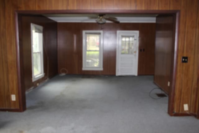 carpeted spare room featuring ceiling fan, wood walls, and plenty of natural light
