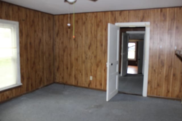 carpeted spare room featuring ceiling fan, wood walls, and plenty of natural light