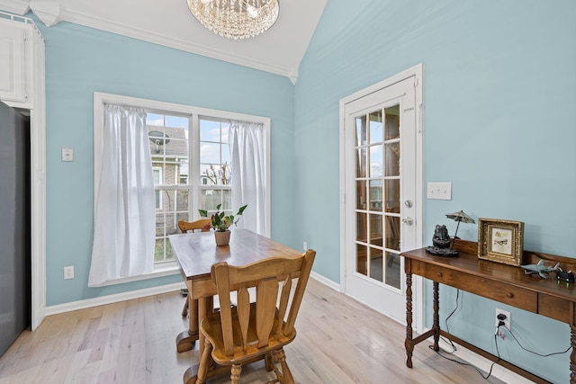 dining space with crown molding, a chandelier, vaulted ceiling, and light wood-type flooring