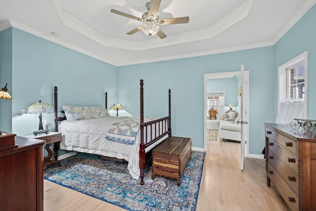 bedroom with multiple windows, a tray ceiling, and light wood-type flooring