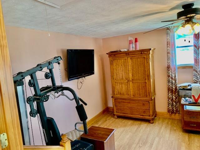 workout room featuring ceiling fan, light hardwood / wood-style floors, and a textured ceiling