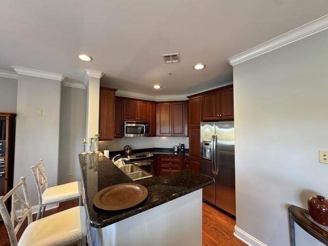 kitchen with sink, dark stone countertops, light wood-type flooring, kitchen peninsula, and stainless steel appliances