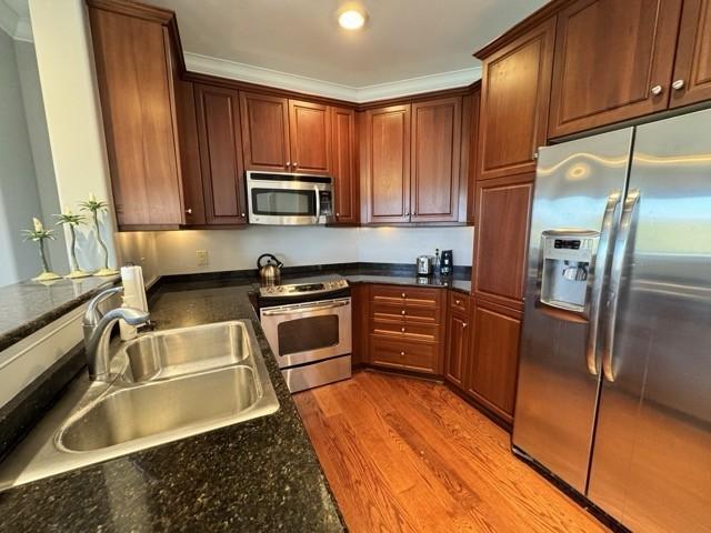 kitchen with dark stone countertops, sink, stainless steel appliances, and light hardwood / wood-style floors