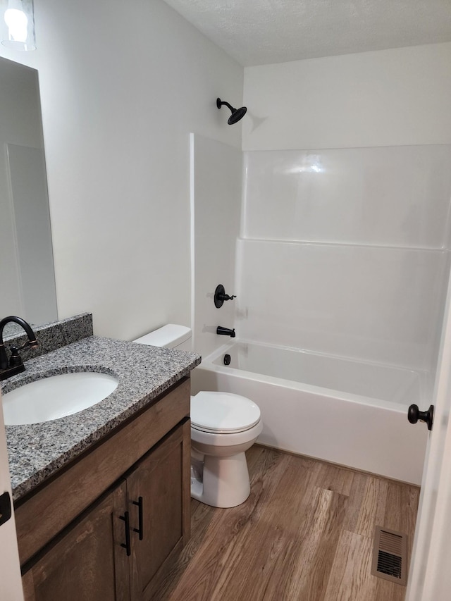 full bathroom featuring hardwood / wood-style flooring, tub / shower combination, vanity, a textured ceiling, and toilet